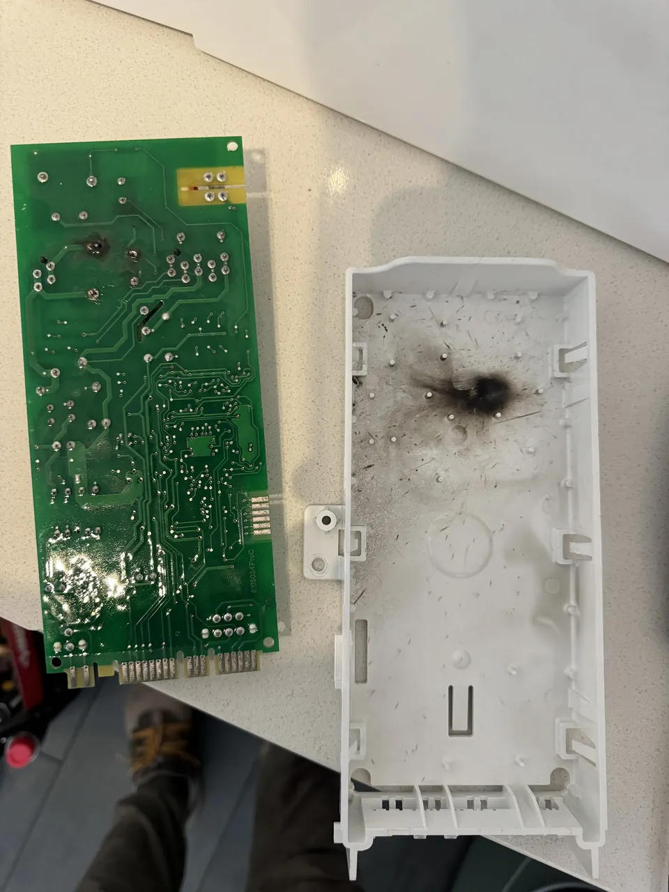 Microwave control board with a burnt track, taken out and laid next to
                         its housing