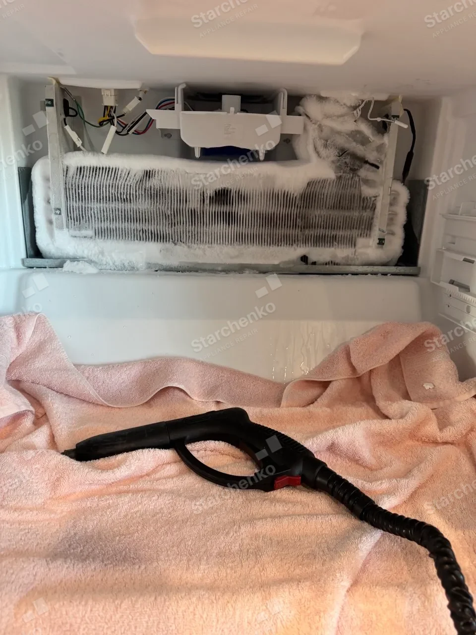 Viking freezer evaporator coil covered in ice with the back panel removed, a steamer and towels laid underneath