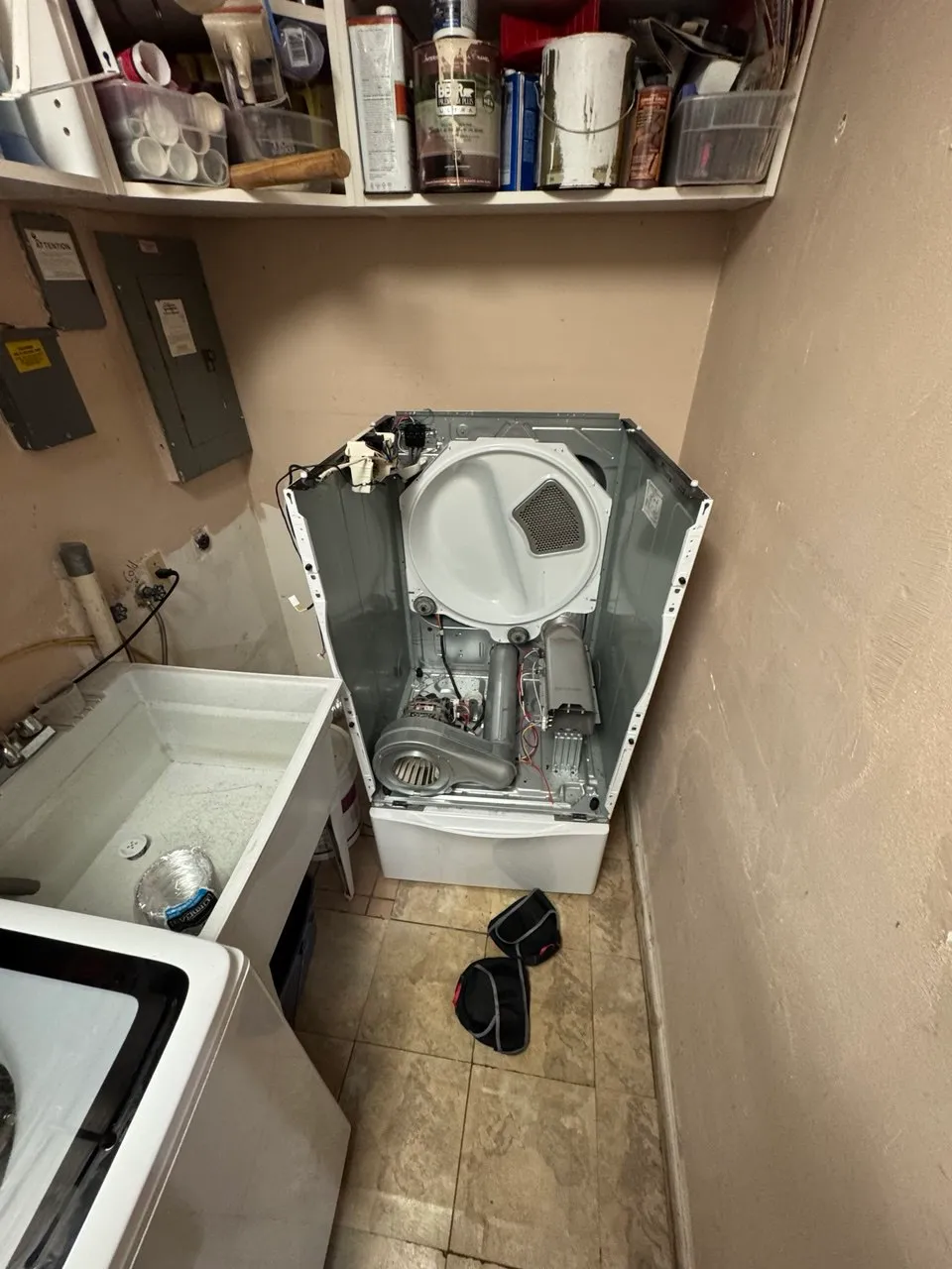 Dryer on a pedestal with the front panel removed: drum, blower housing and heating element exposed