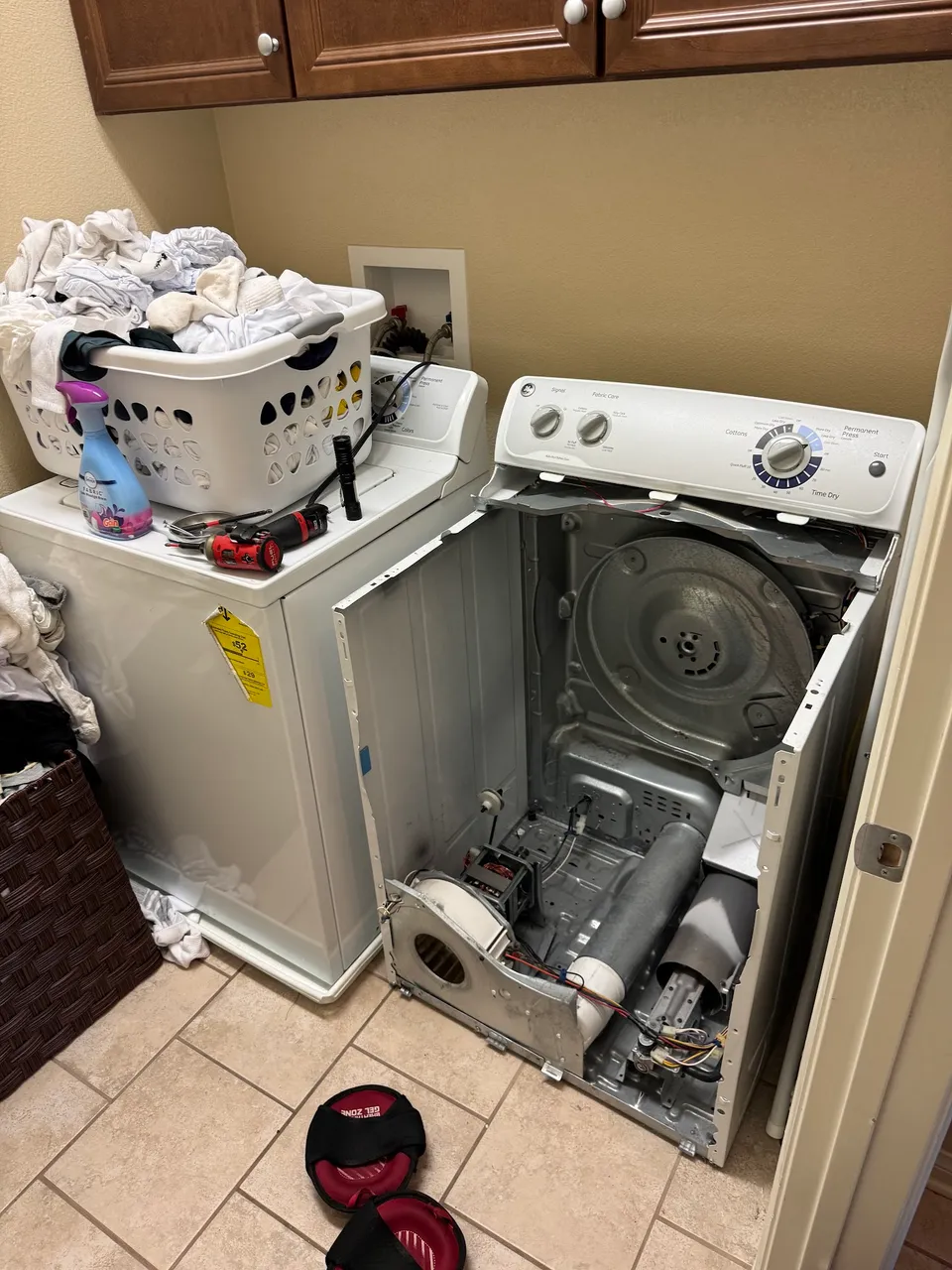 GE dryer with the front panel off beside a top-load washer, drum and blower visible