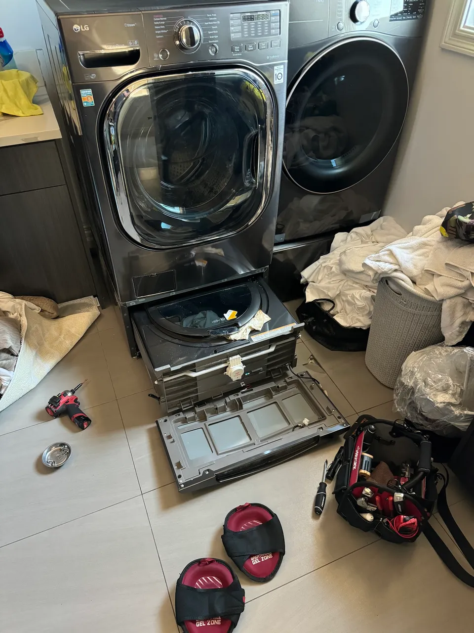 Stacked LG laundry unit with the lower machine opened and parts on the floor