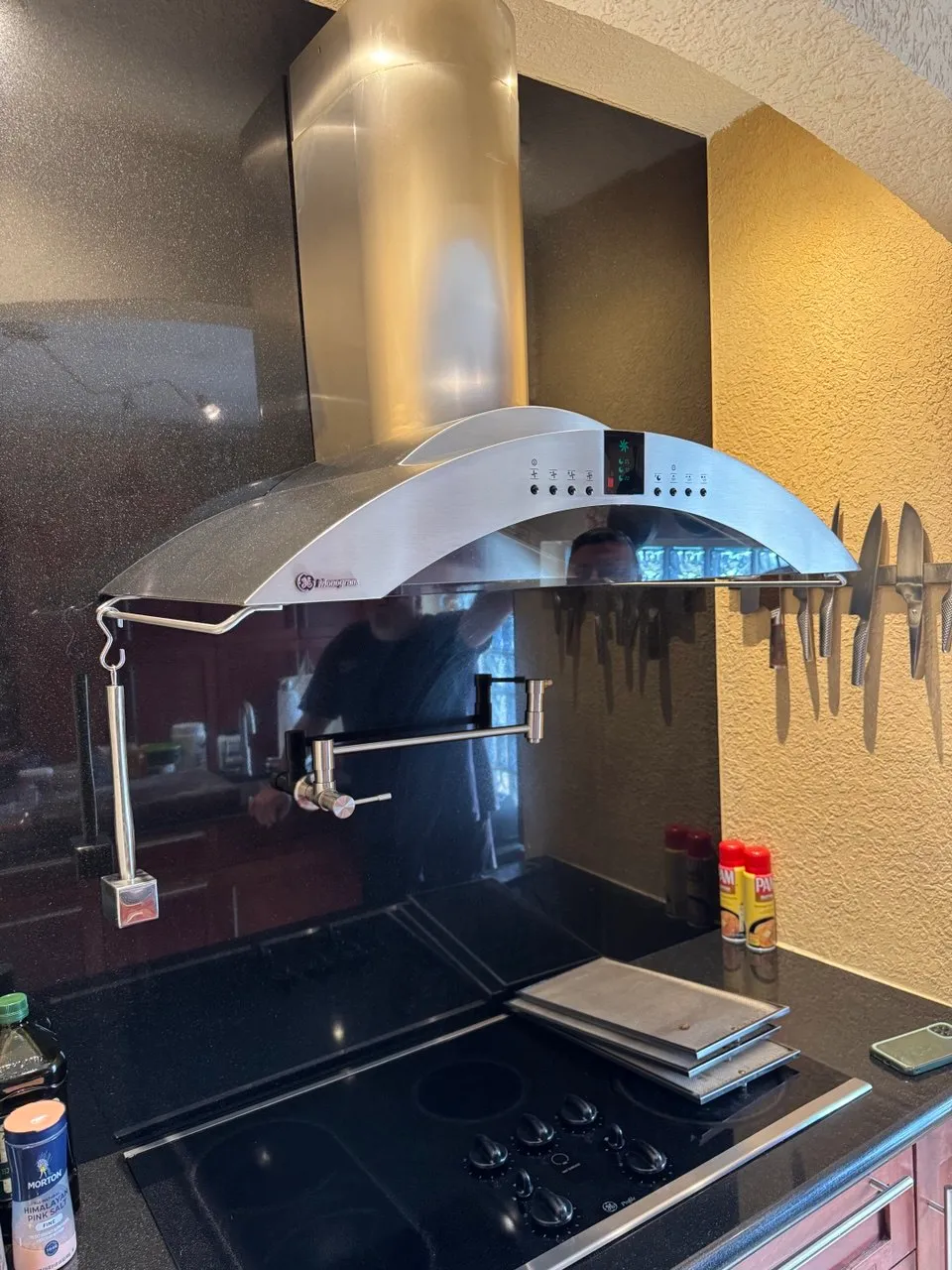 Stainless range hood above a black glass cooktop