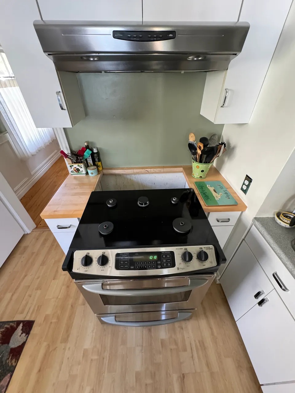 Stainless electric range under a hood between white cabinets