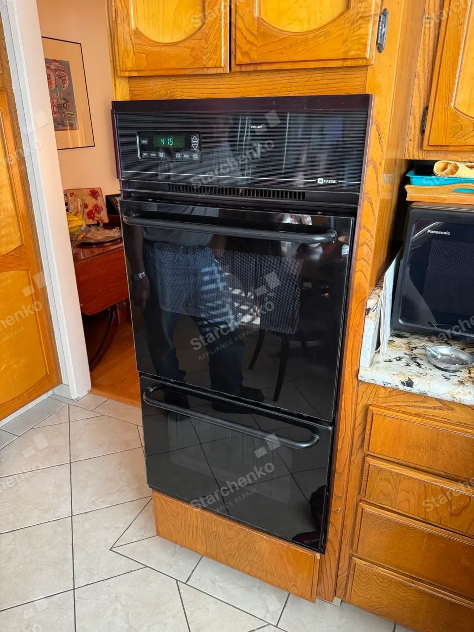 Black Maytag built-in wall oven in oak cabinets with a microwave beside it