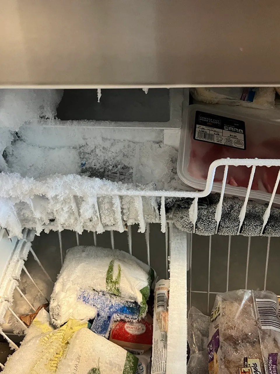 Freezer compartment iced over with frost across the shelves and baskets