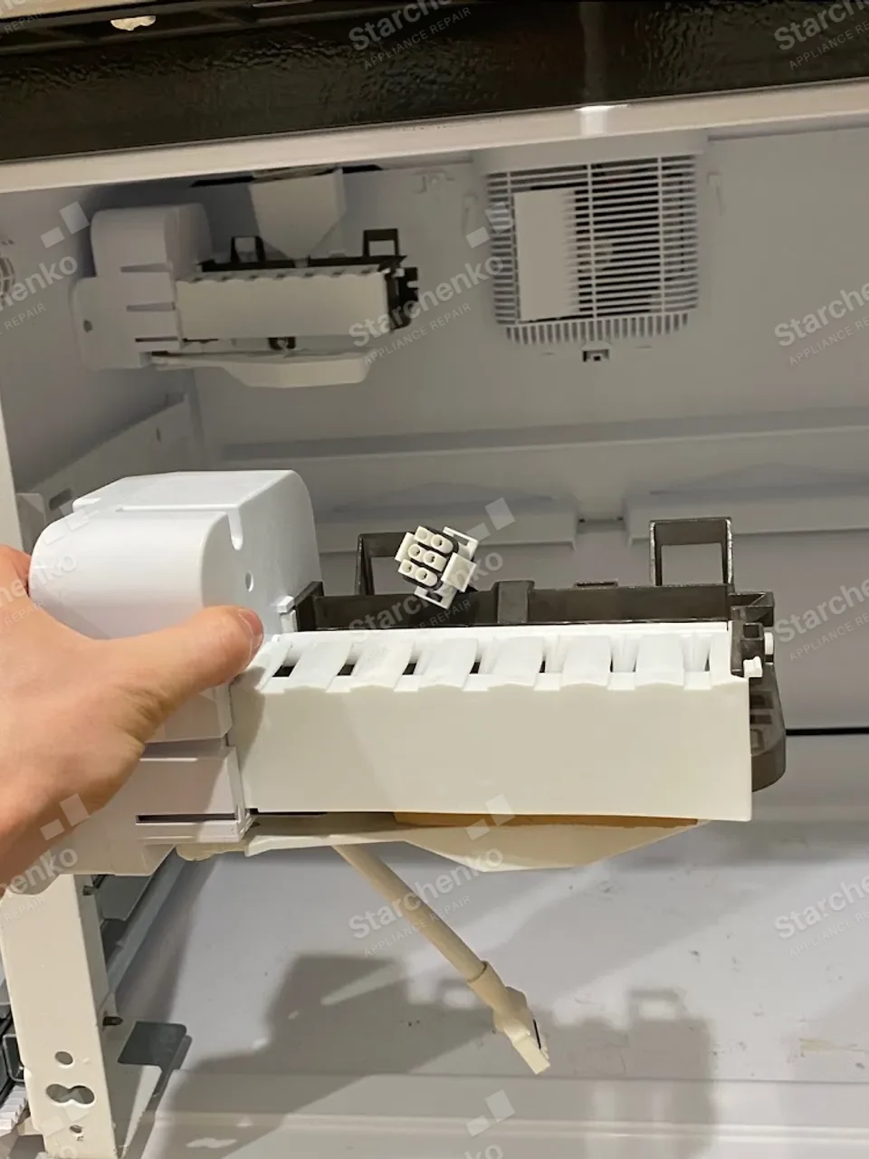 Hand pulling the Whirlpool ice maker tray module out of the freezer drawer