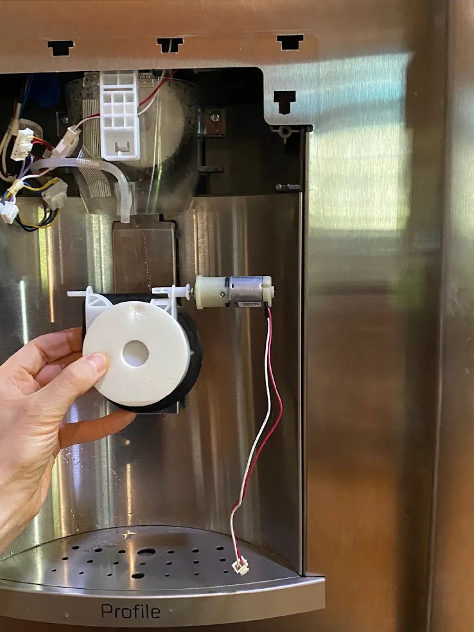 Hand holding the ice maker dispenser auger part at the refrigerator door