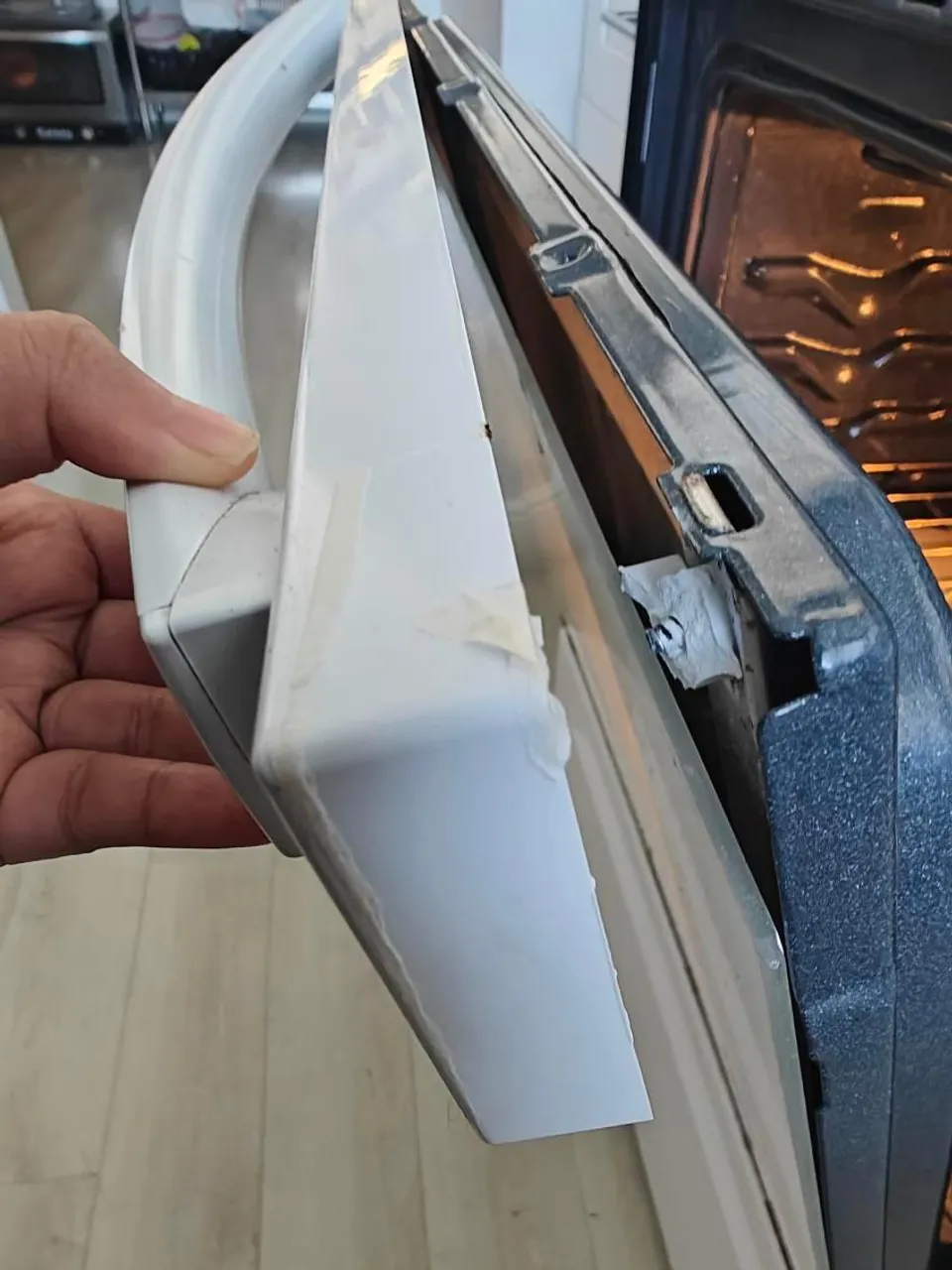 Hand holding the oven door panel taken off during the repair