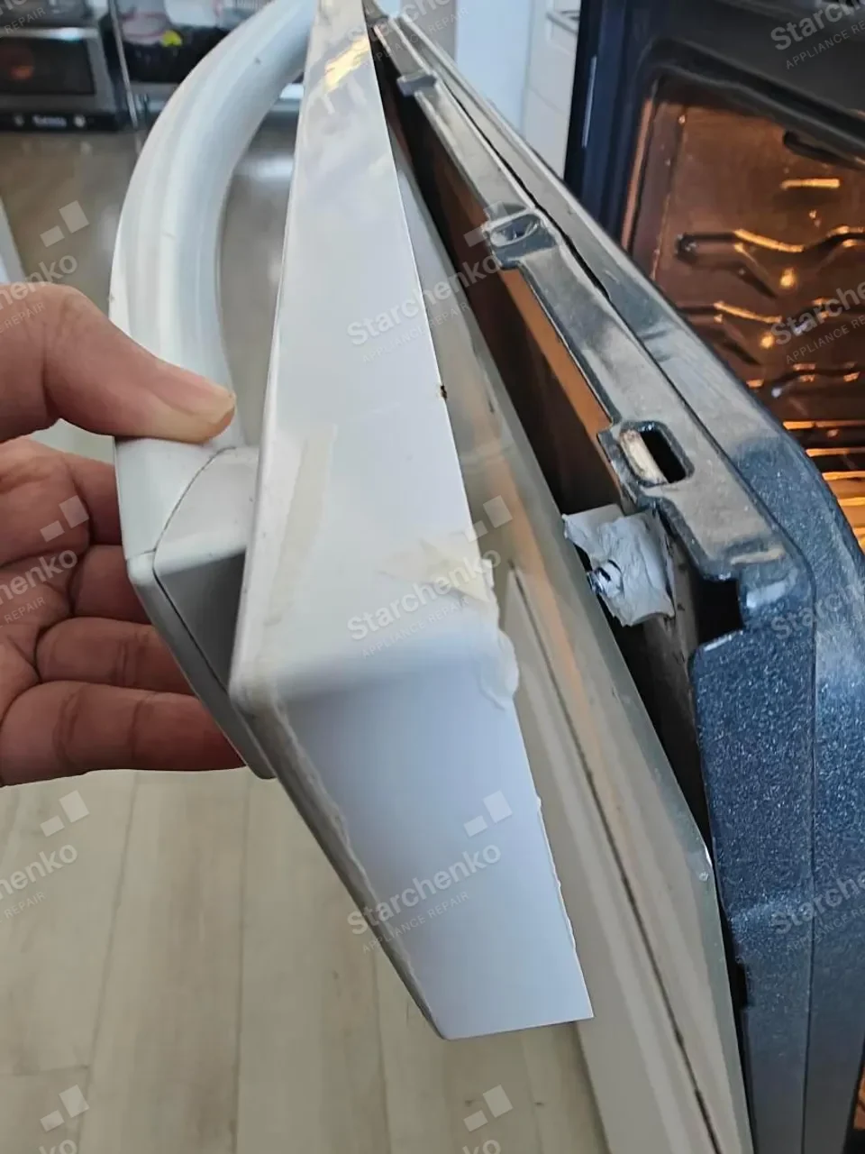 Hand holding the GE oven door panel taken off during the repair