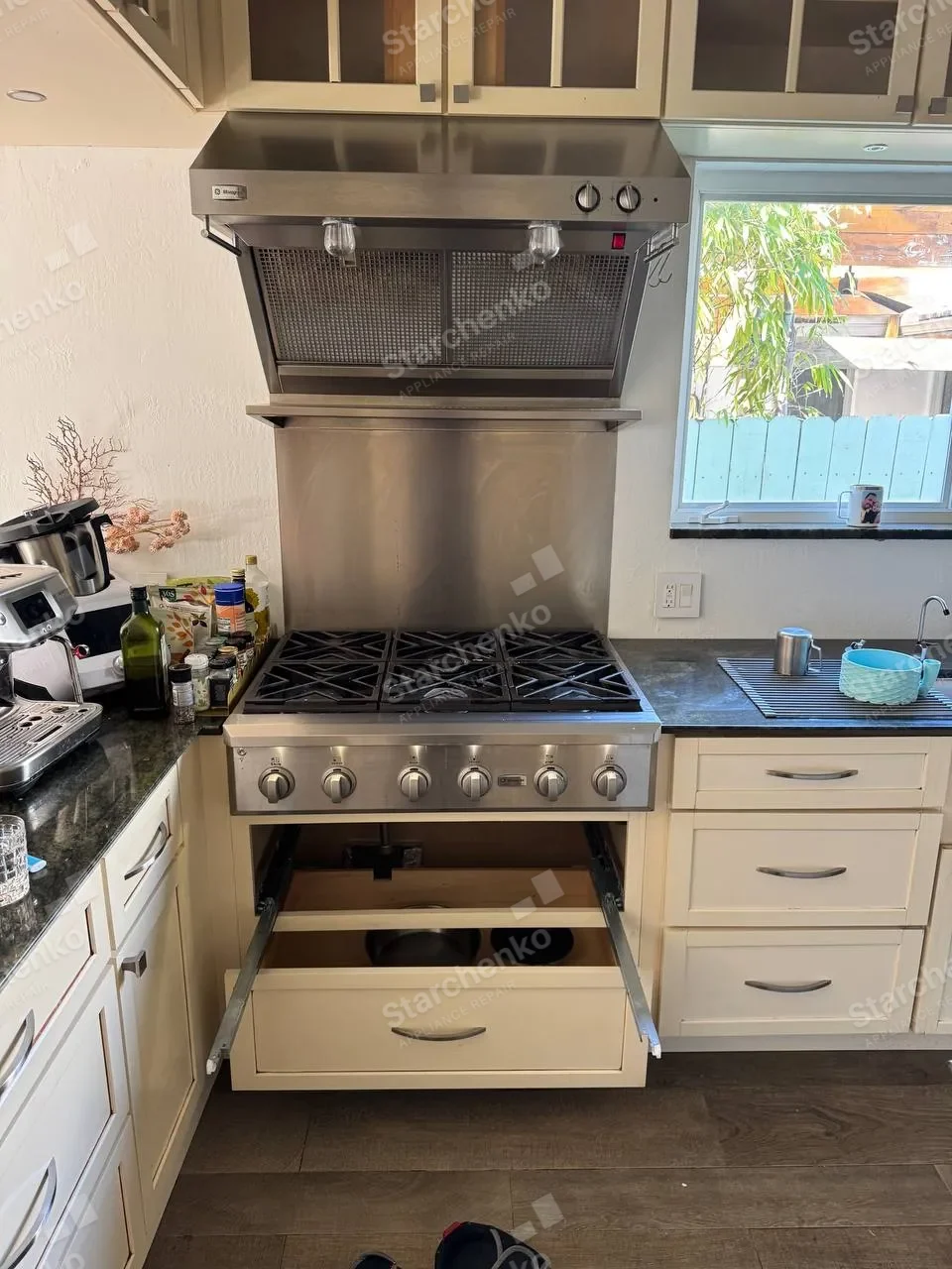 Pro-style GE Monogram gas range under a stainless hood with the drawer pulled open