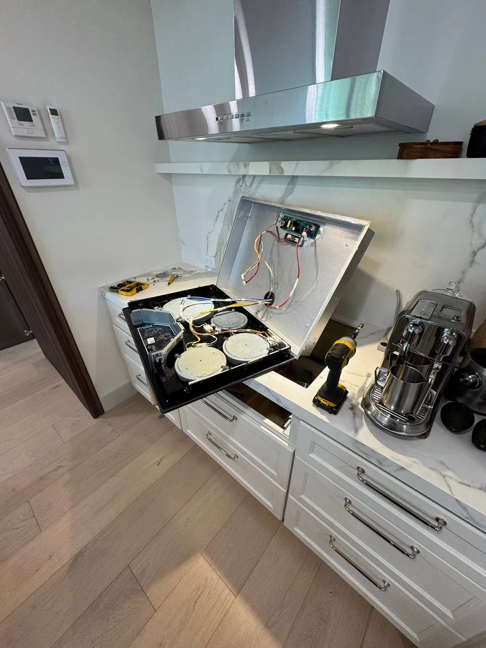 Electric cooktop lifted out of the countertop with the glass raised, exposing heating elements and control board