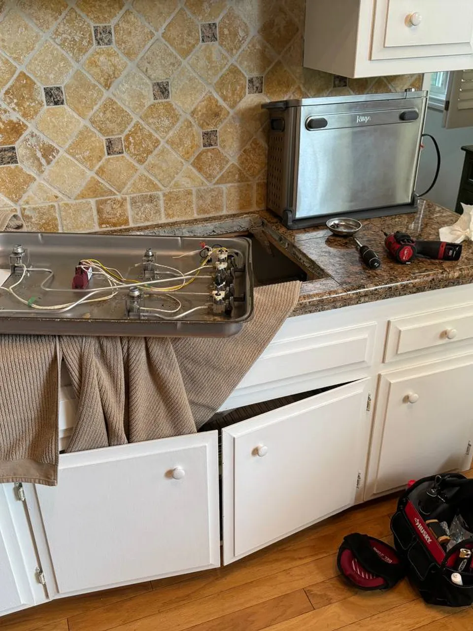 Gas cooktop removed from the countertop and placed on a towel with valves and wiring exposed underneath