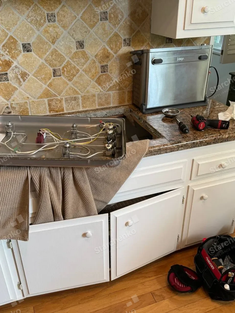 Whirlpool gas cooktop removed from the countertop and placed on a towel with valves and wiring exposed underneath