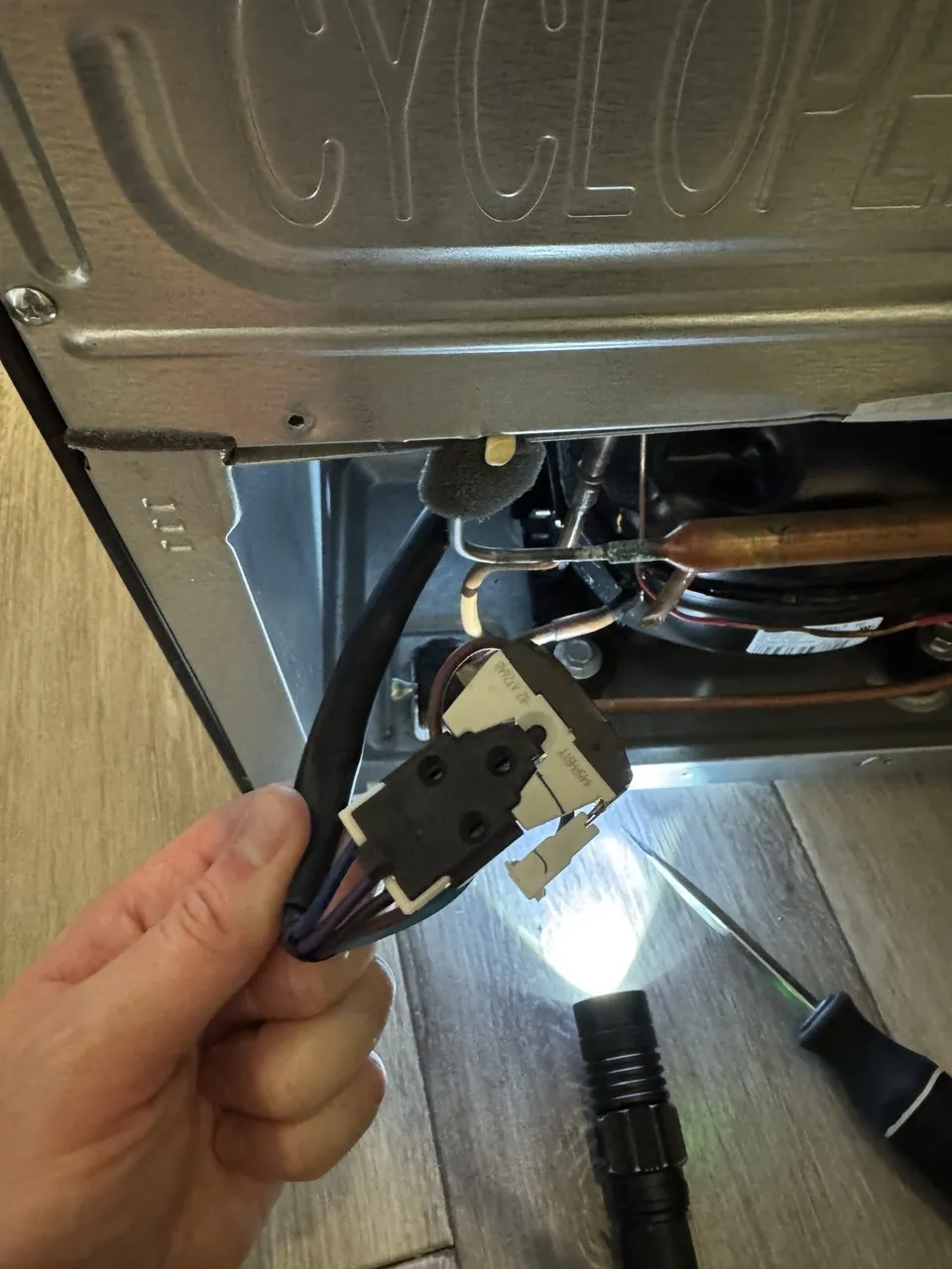 Back of a refrigerator opened with the compressor start relay in hand