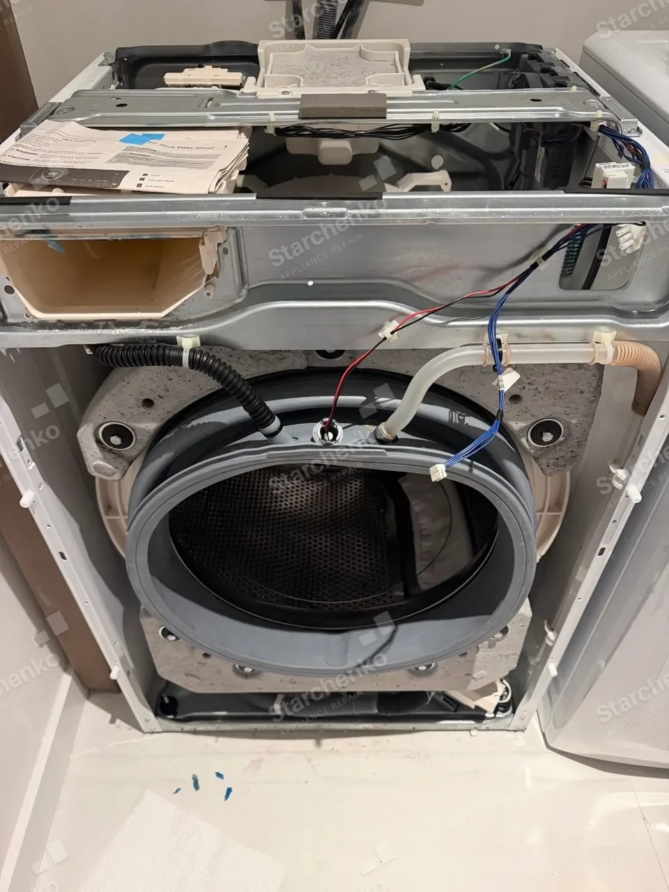 Samsung washer opened up with the outer tub, water hoses and drum exposed