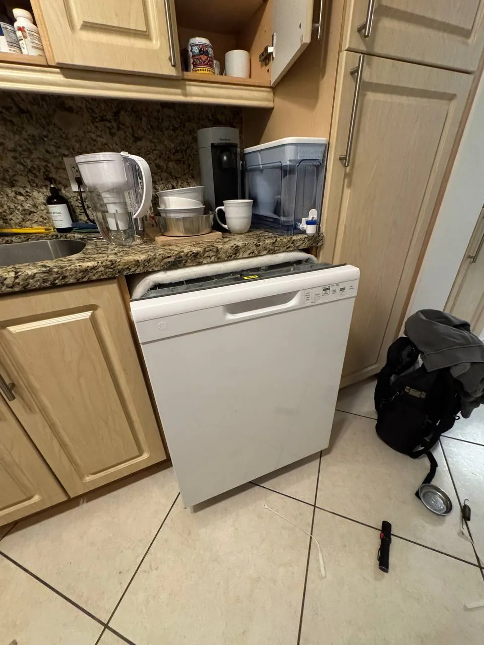 White GE dishwasher pulled out from under a granite counter with its top insulation off