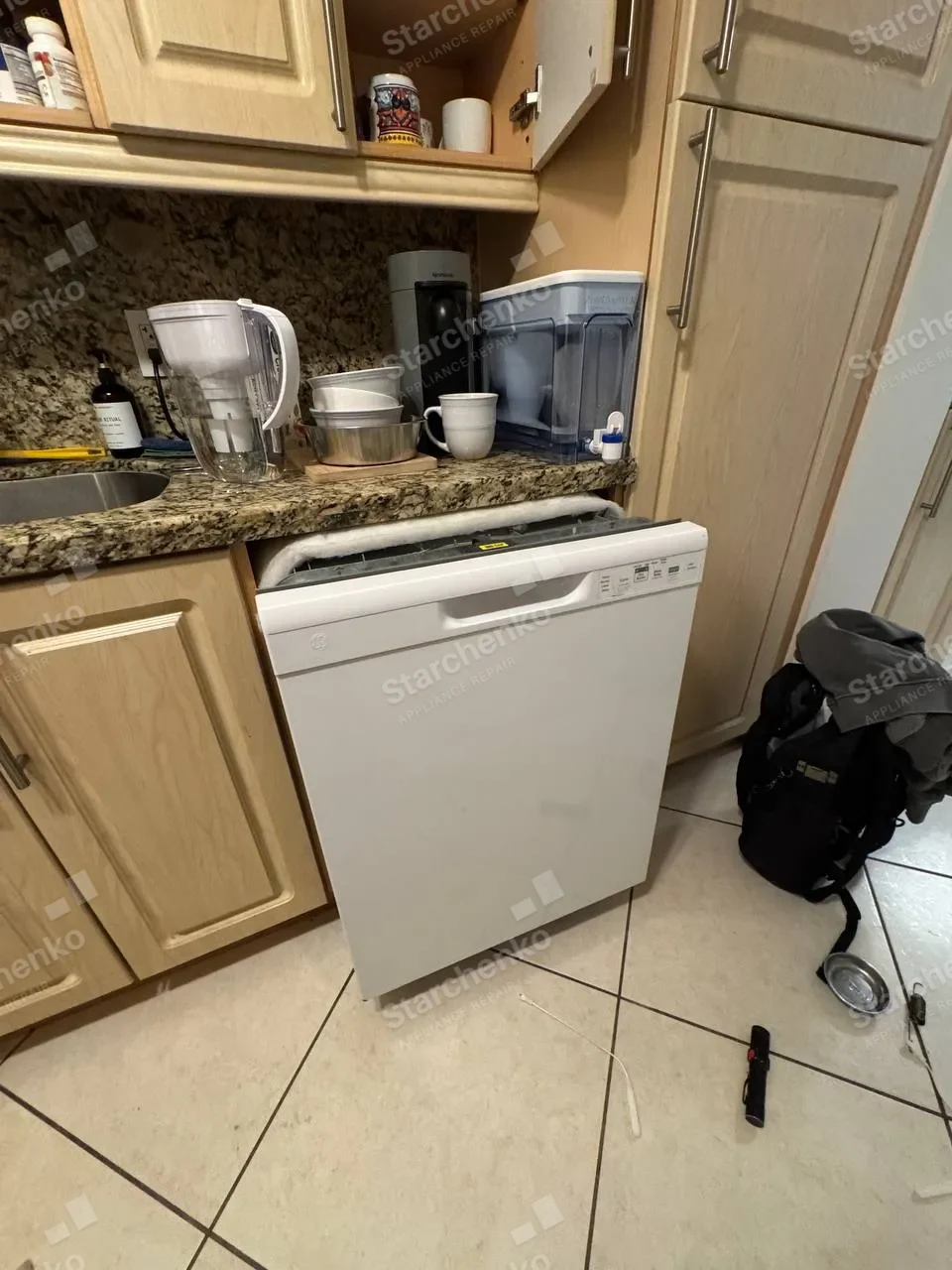White GE dishwasher pulled out from under a granite counter with its top insulation off
