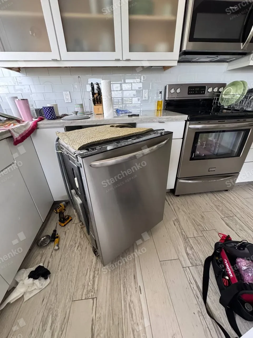 Stainless Frigidaire dishwasher pulled out from under the counter with its insulation mat lying on top