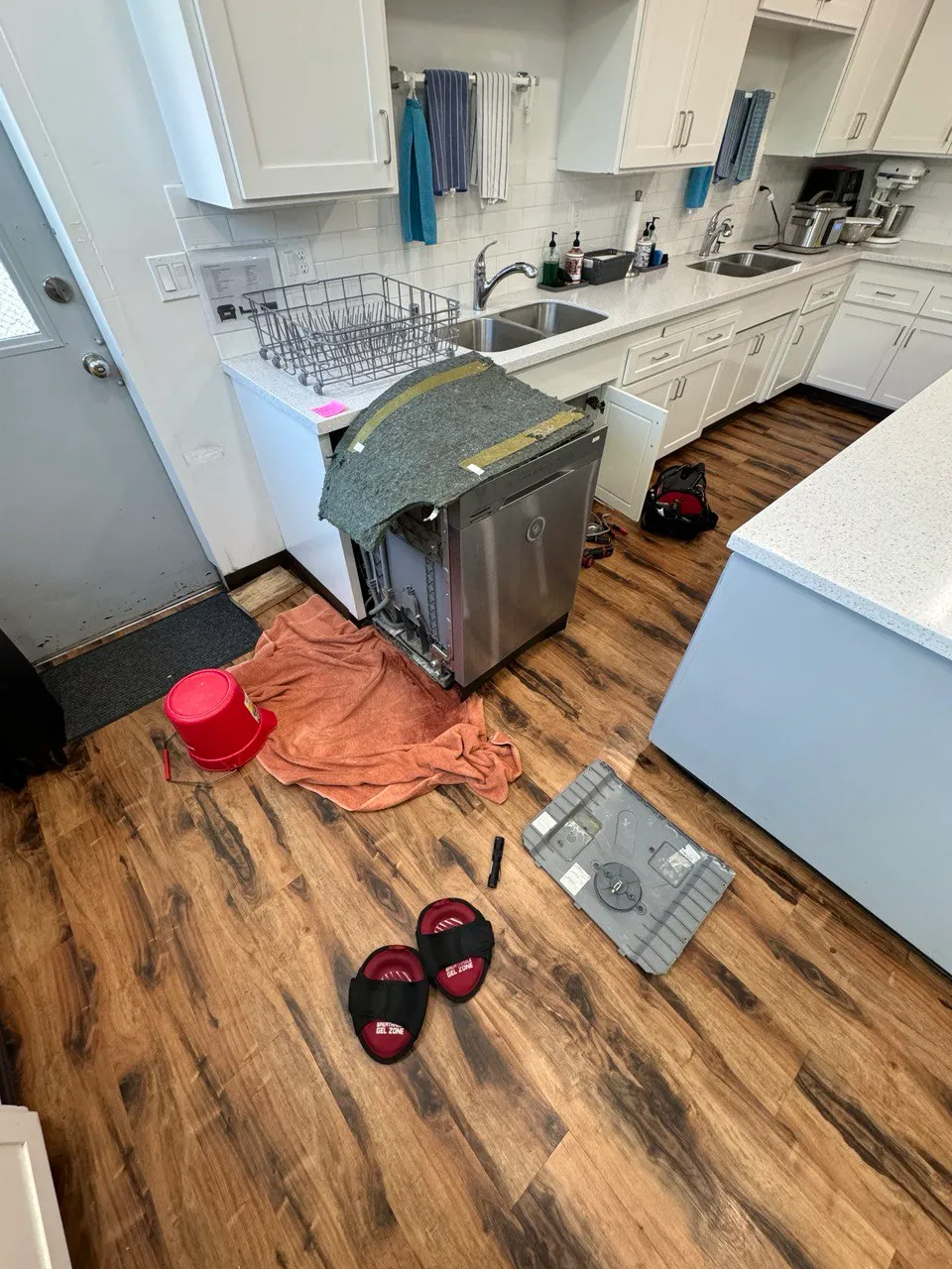 Stainless dishwasher pulled out with its base pan removed and set on the kitchen floor