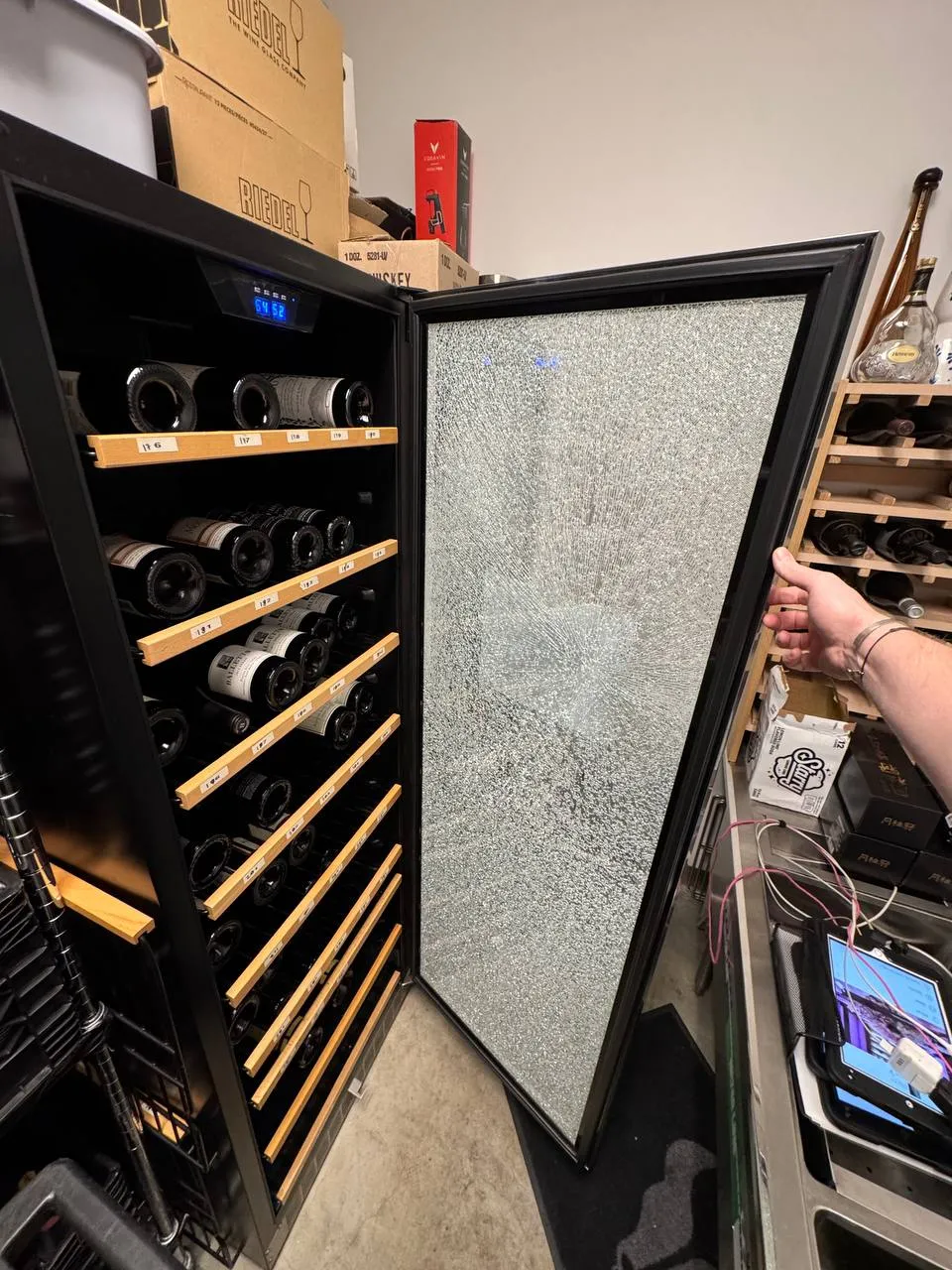 Freestanding wine cooler with its glass door shattered and bottles on the wooden racks