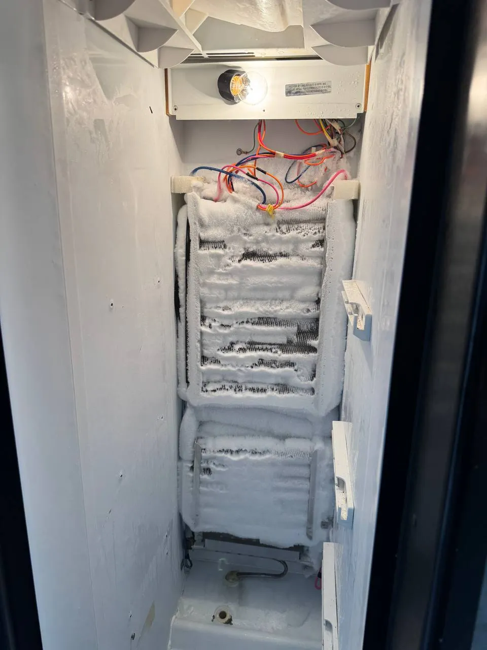 Freezer compartment with the rear panel removed: the evaporator coil is solid with frost and the wiring is exposed