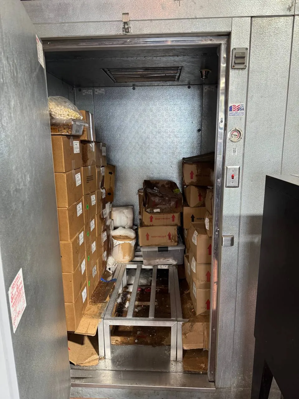 Walk-in freezer with its insulated door open, ceiling evaporator and stored boxes visible