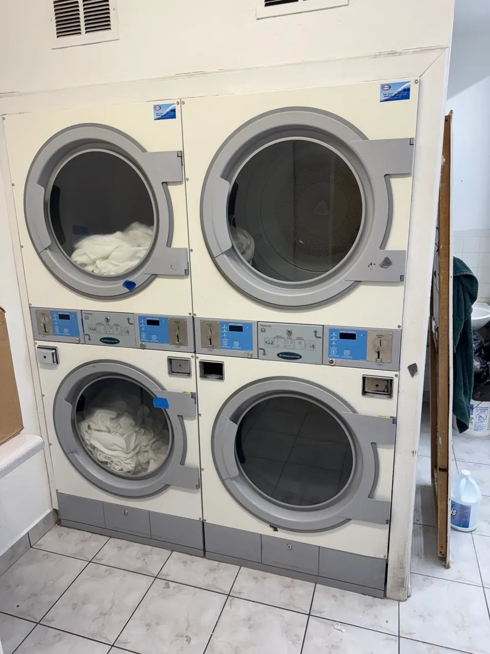 Four coin-operated Wascomat commercial dryers in a shared laundry room