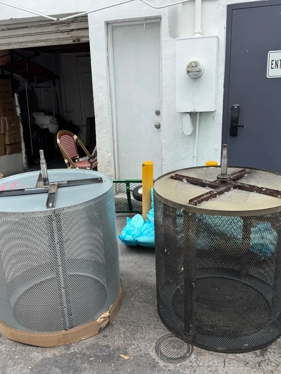 Two commercial dryer drums removed outdoors beside an Alliance Laundry Systems box