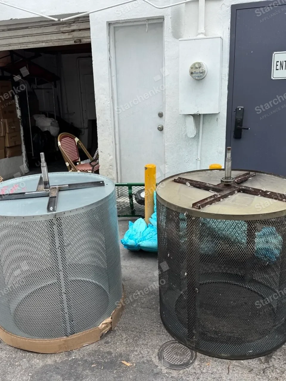 Two perforated Huebsch commercial dryer drums removed and standing outdoors by a service door