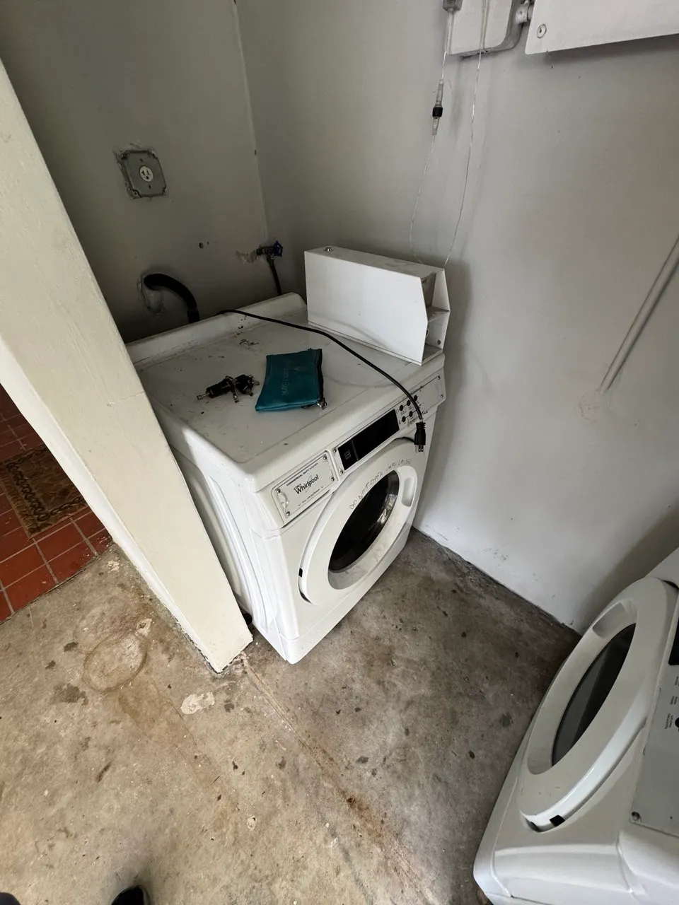 Coin-operated Whirlpool commercial washer with the top panel removed in a shared laundry room