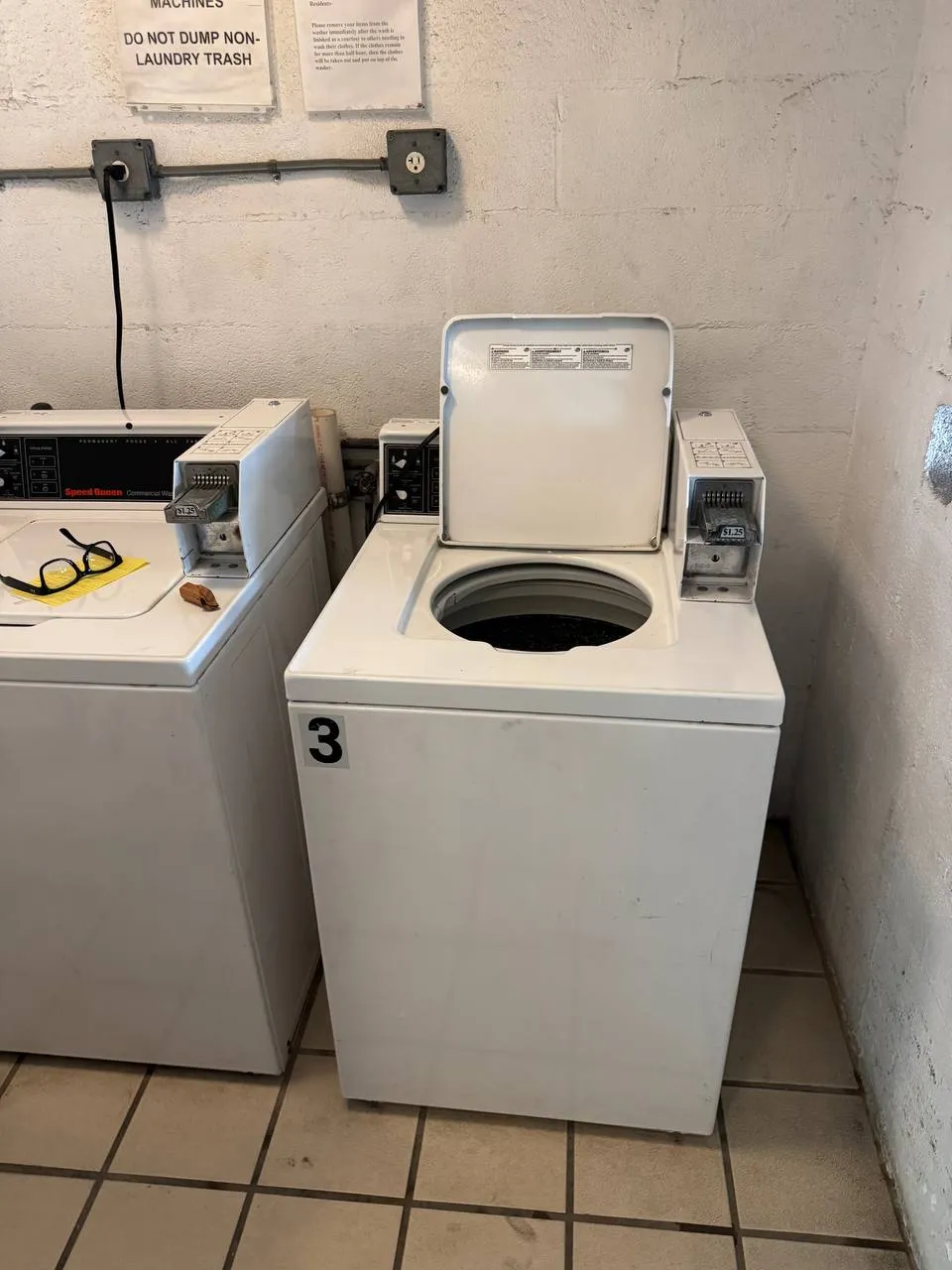 Two commercial washers by Speed Queen with coin controls and one top-load lid open