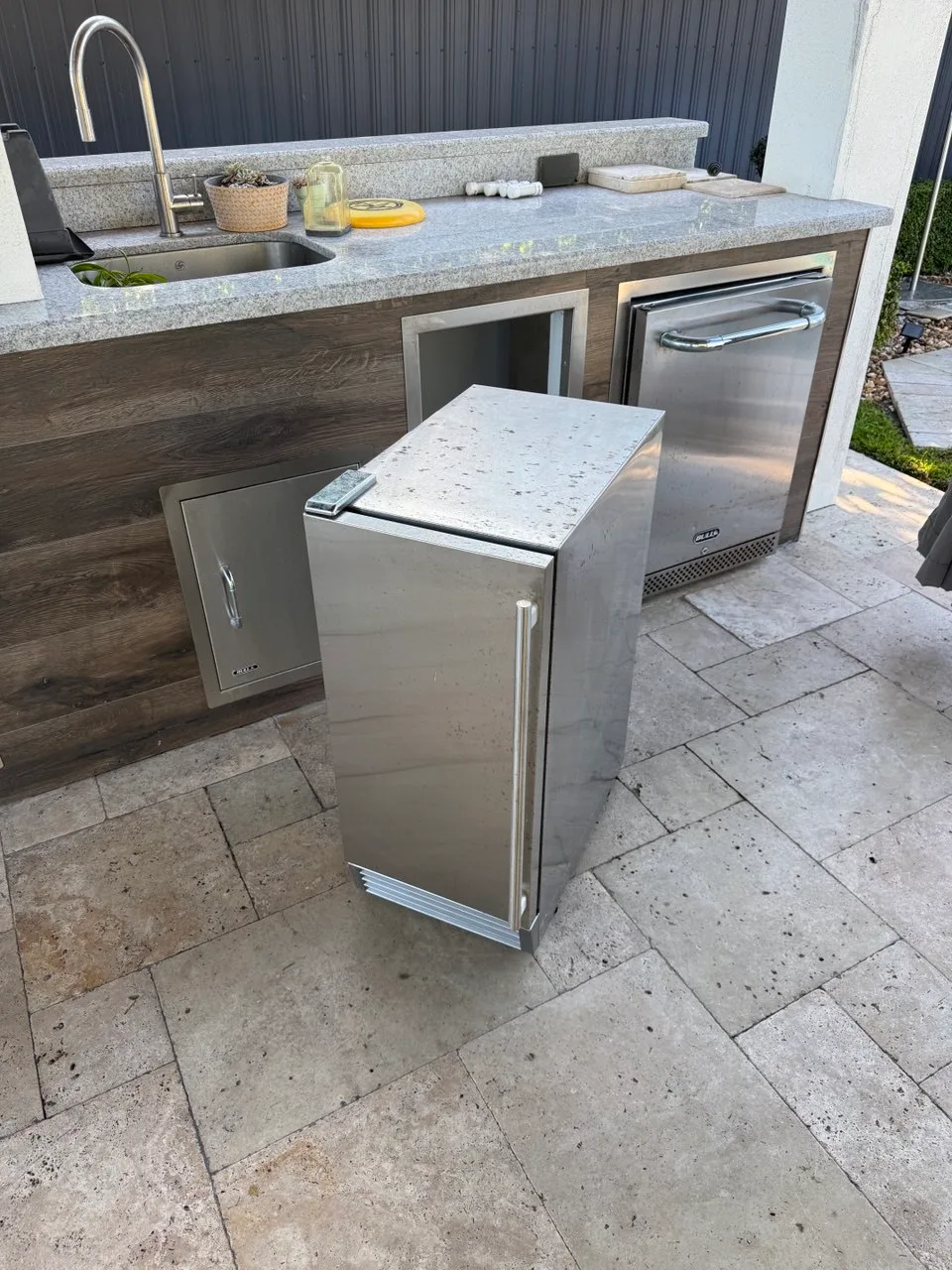 Stainless undercounter ice maker pulled out from an outdoor kitchen cabinet