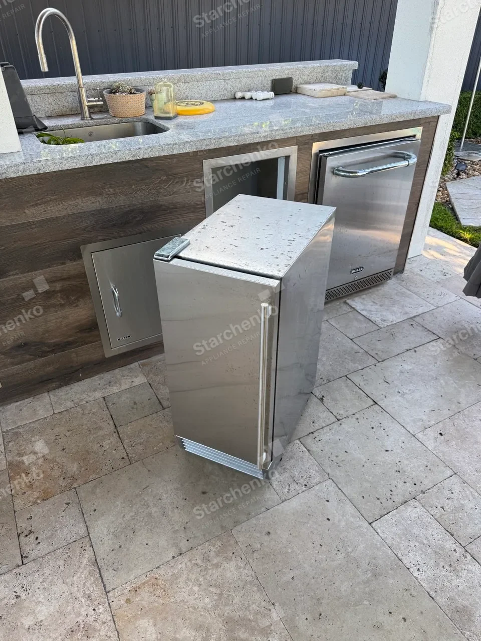 Stainless undercounter U-Line ice maker pulled out from an outdoor kitchen cabinet