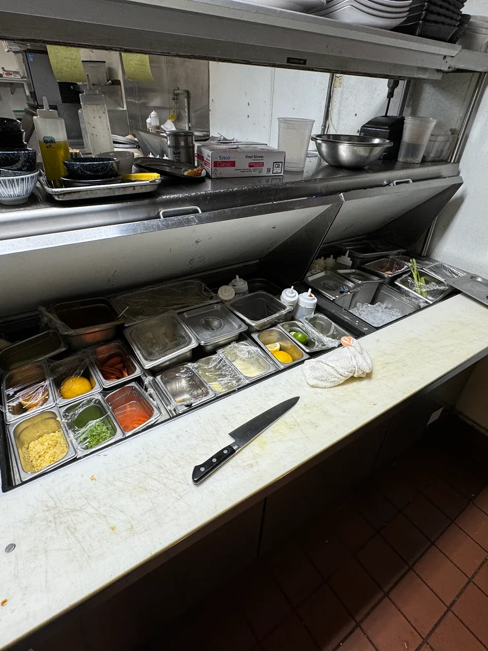 Commercial refrigeration prep table with ingredient wells open in a restaurant kitchen