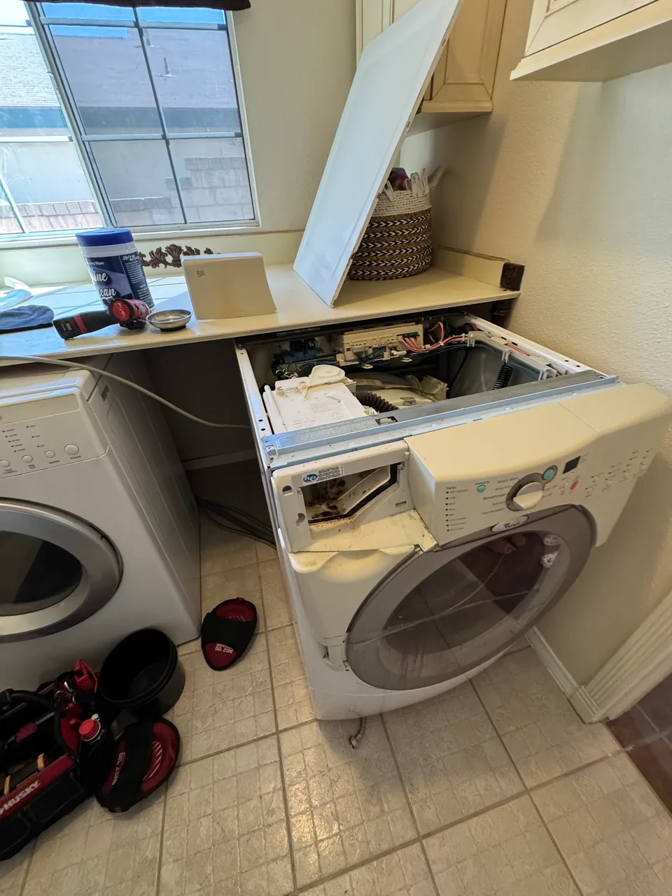 Front-load washer under a counter with its top removed for repair