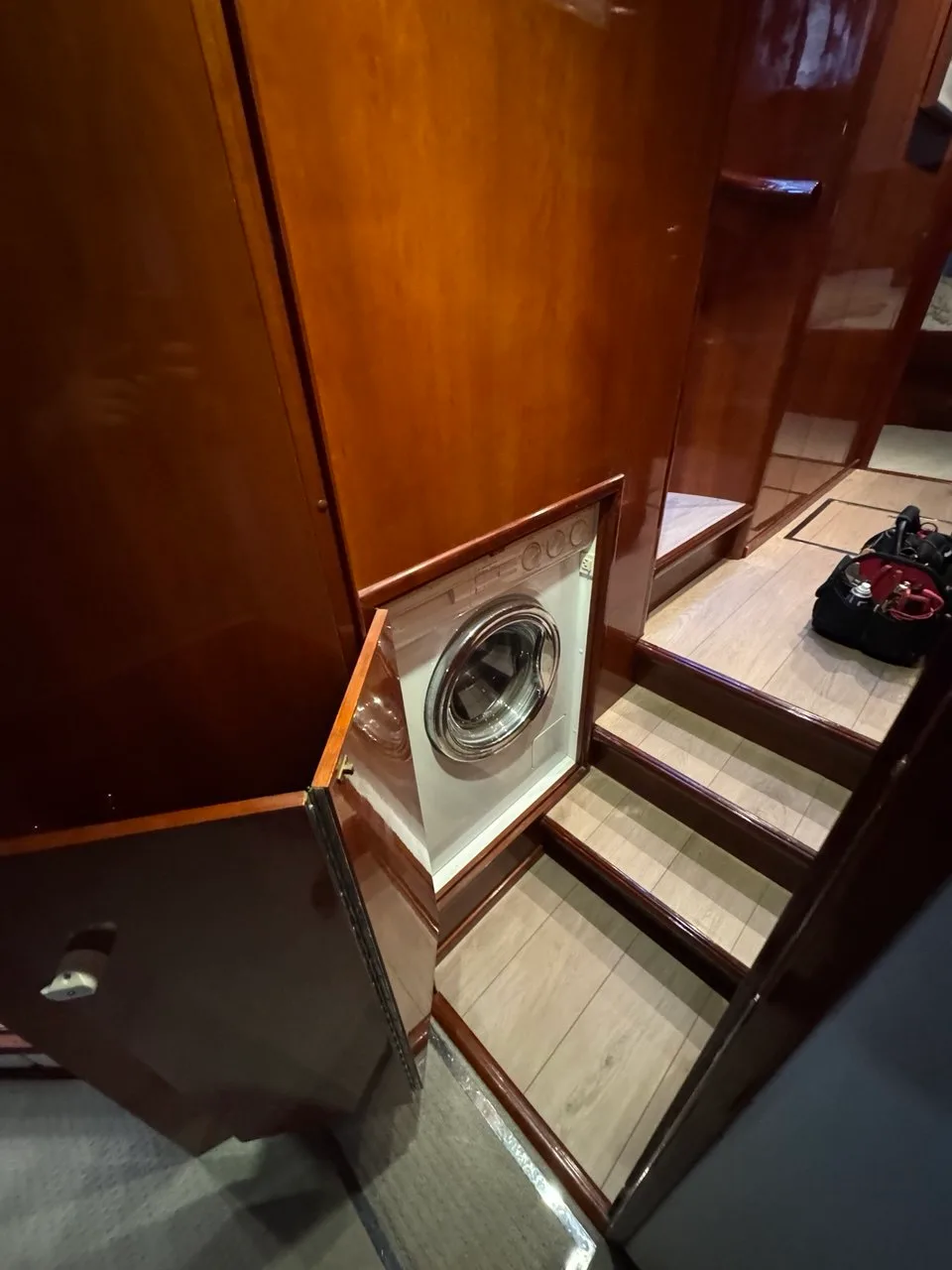 Front-load washer mounted behind an open wood cabinet door on a boat