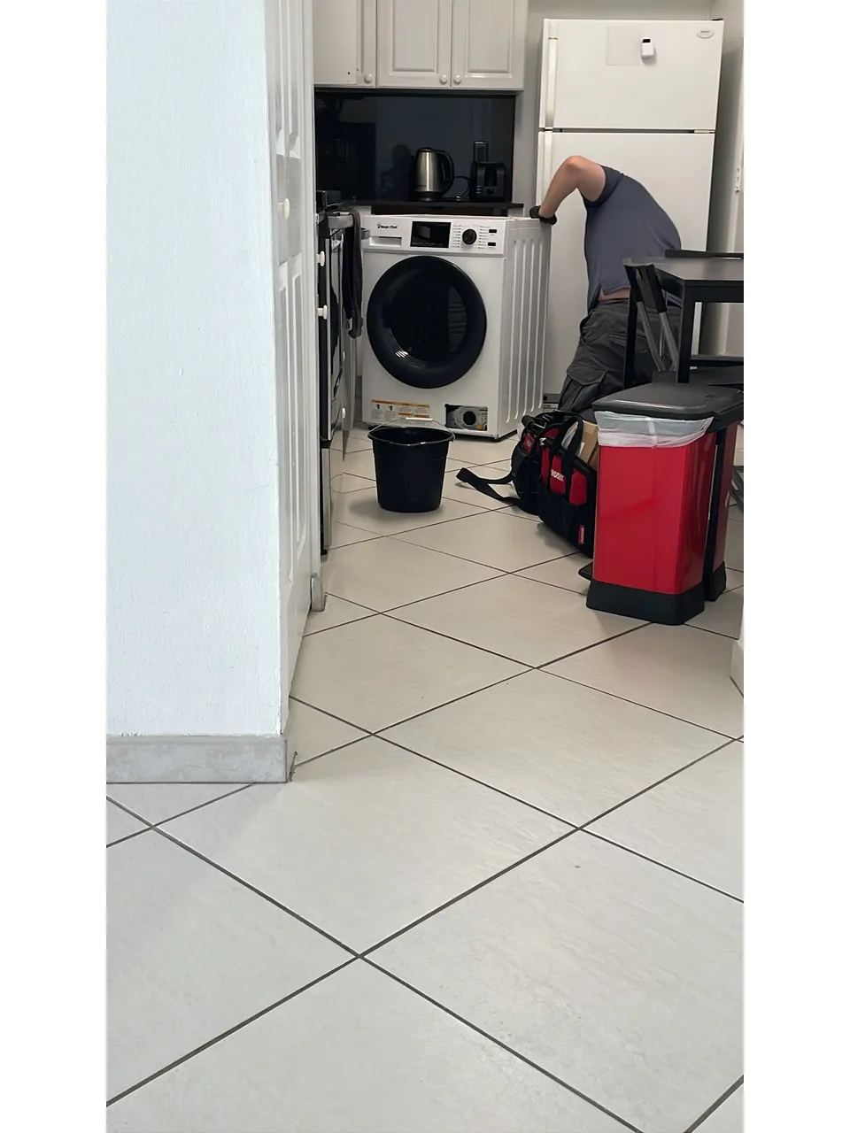 Front-load washer-dryer combo with its lower service port open while a technician works beside it