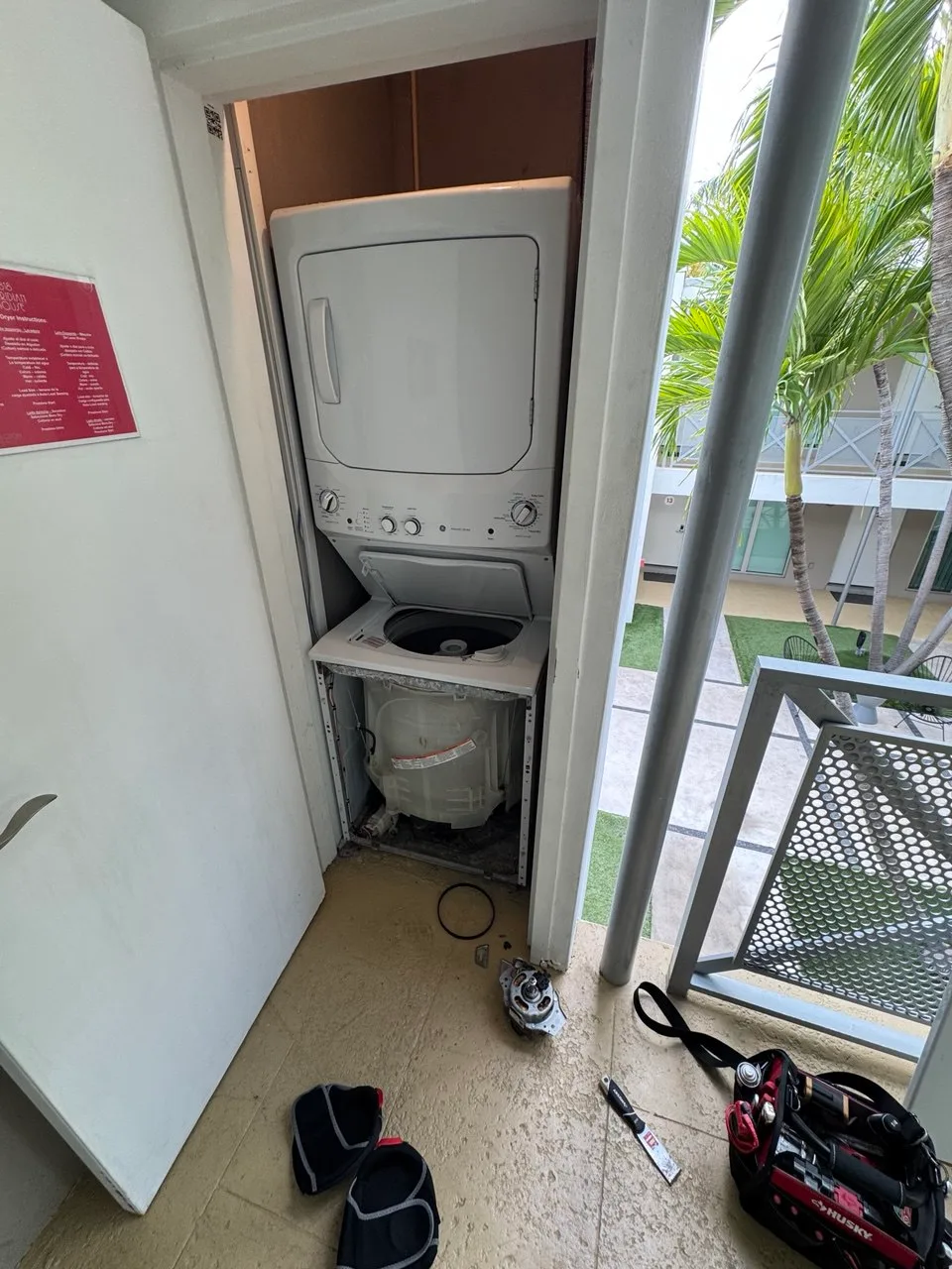 Stacked washer-dryer with the washer front panel removed and drive motor on the floor