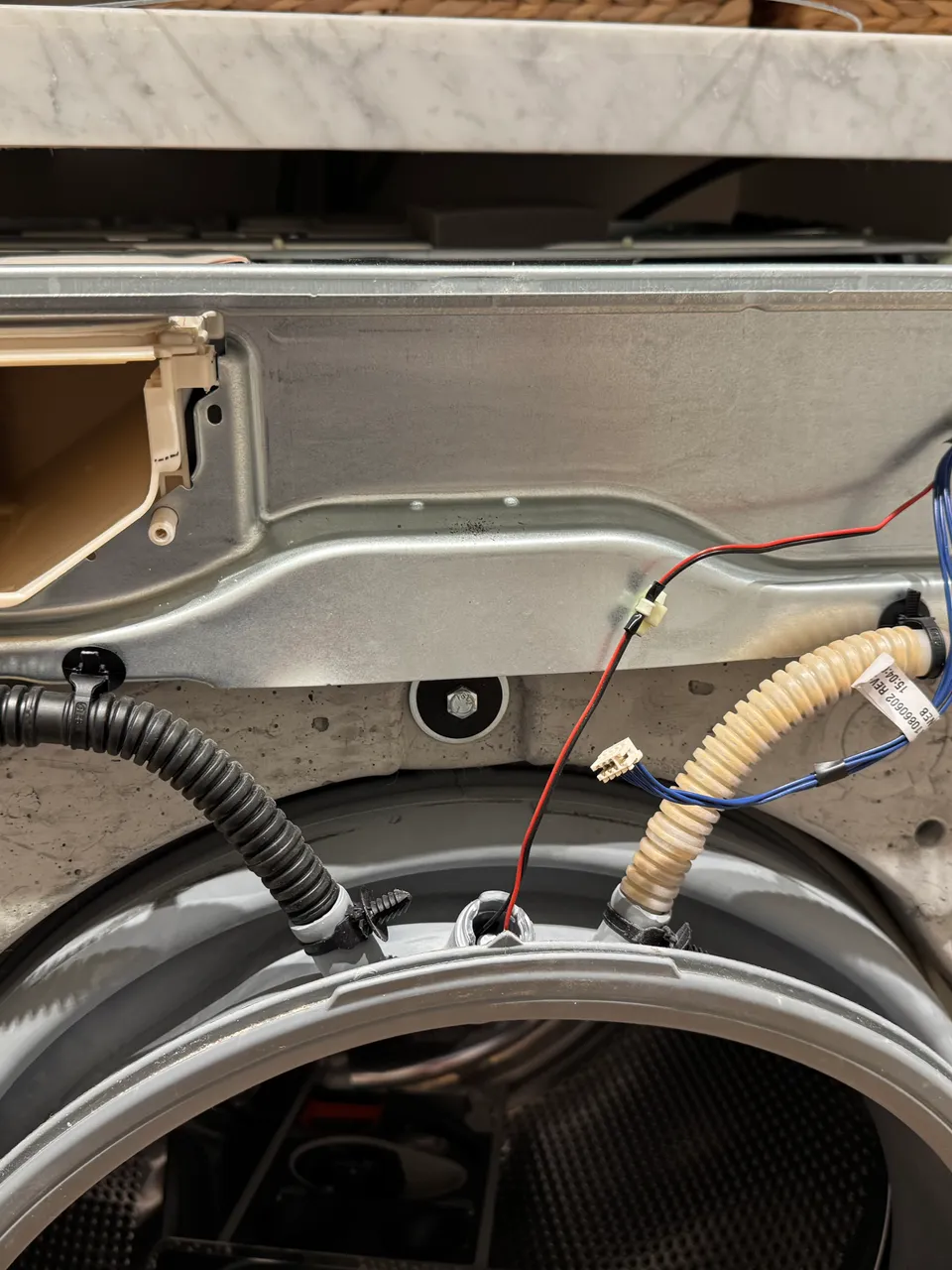 Front-load washer with the top panel removed, detergent dispenser housing, door boot and hoses exposed