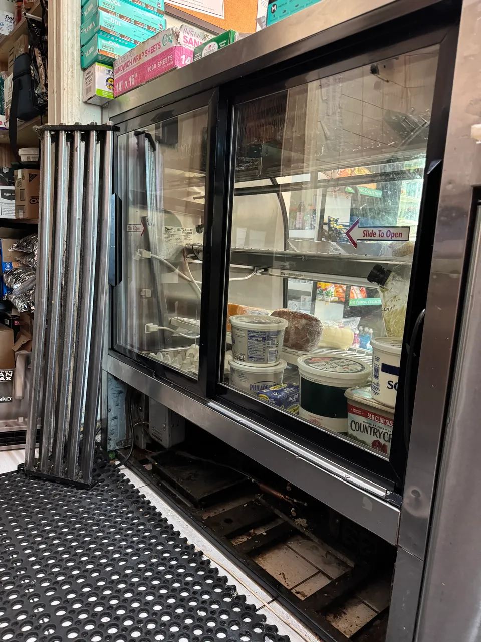 Commercial deli case with the lower grille removed and the condenser exposed