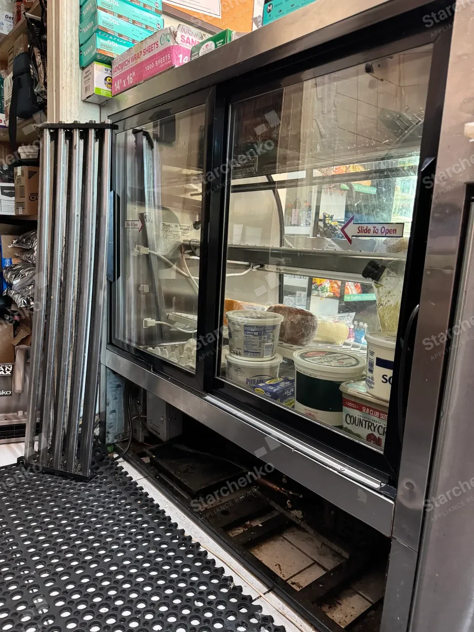 True commercial deli case with the lower grille removed and the condenser exposed