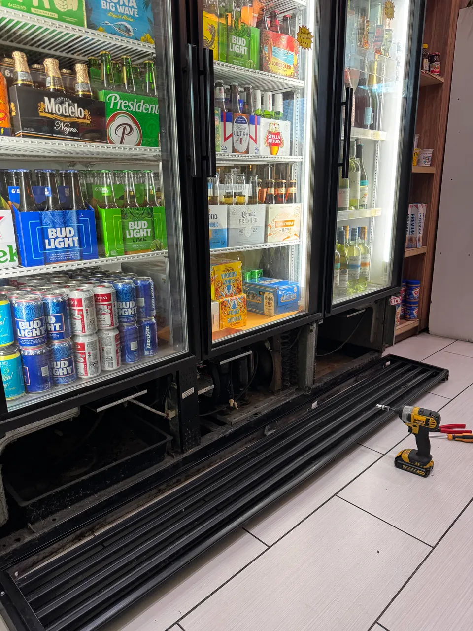 Three-door commercial beverage cooler with the bottom grille removed and lying on the floor