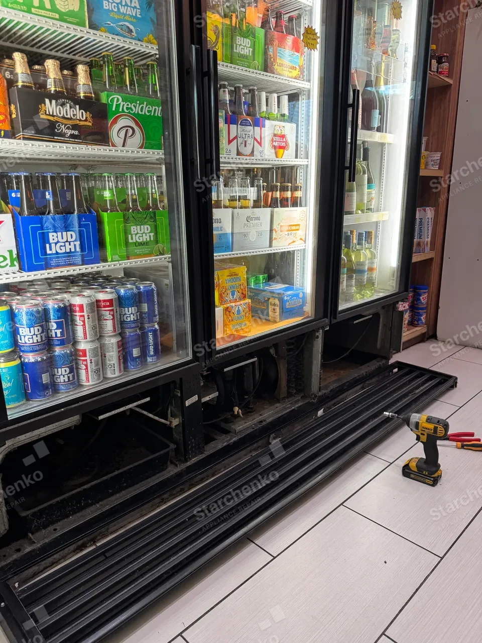 Three-door True commercial beverage cooler with the bottom grille removed and lying on the floor