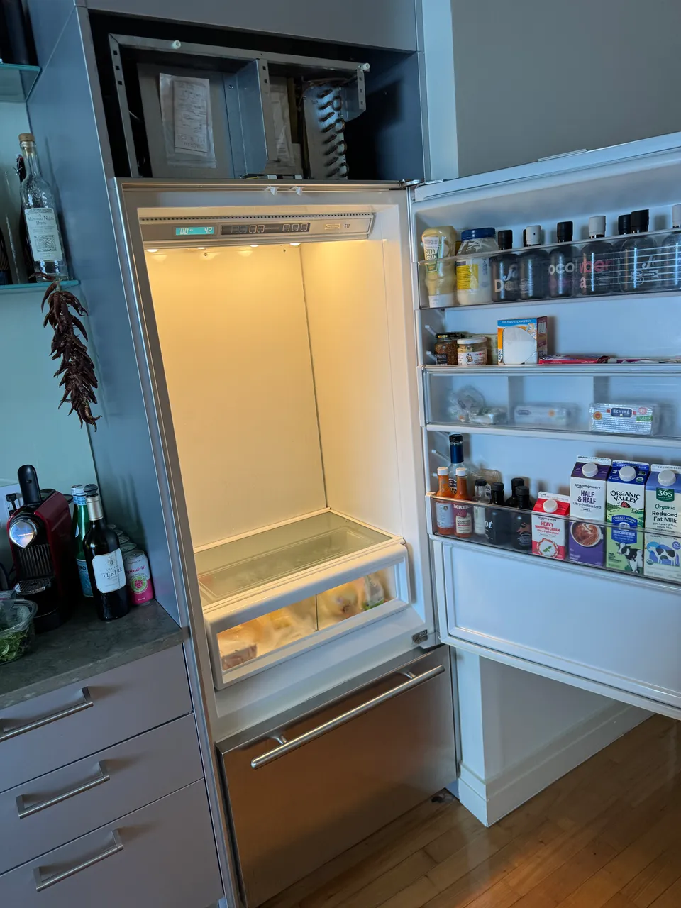 Built-in refrigerator with the top compressor compartment open and the fresh-food section empty