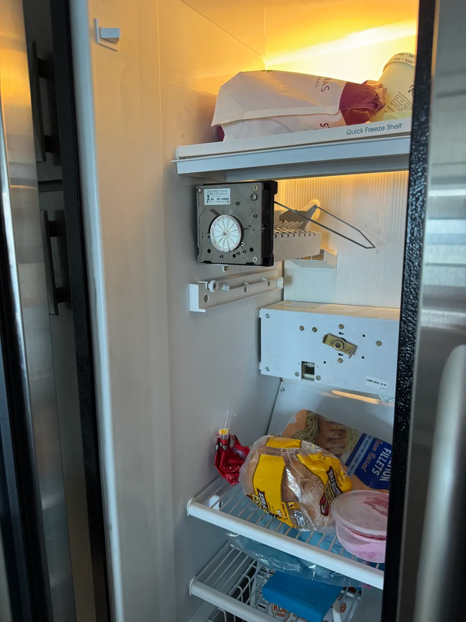 Freezer compartment of a side-by-side refrigerator with the ice maker module unbolted and resting on the shelf