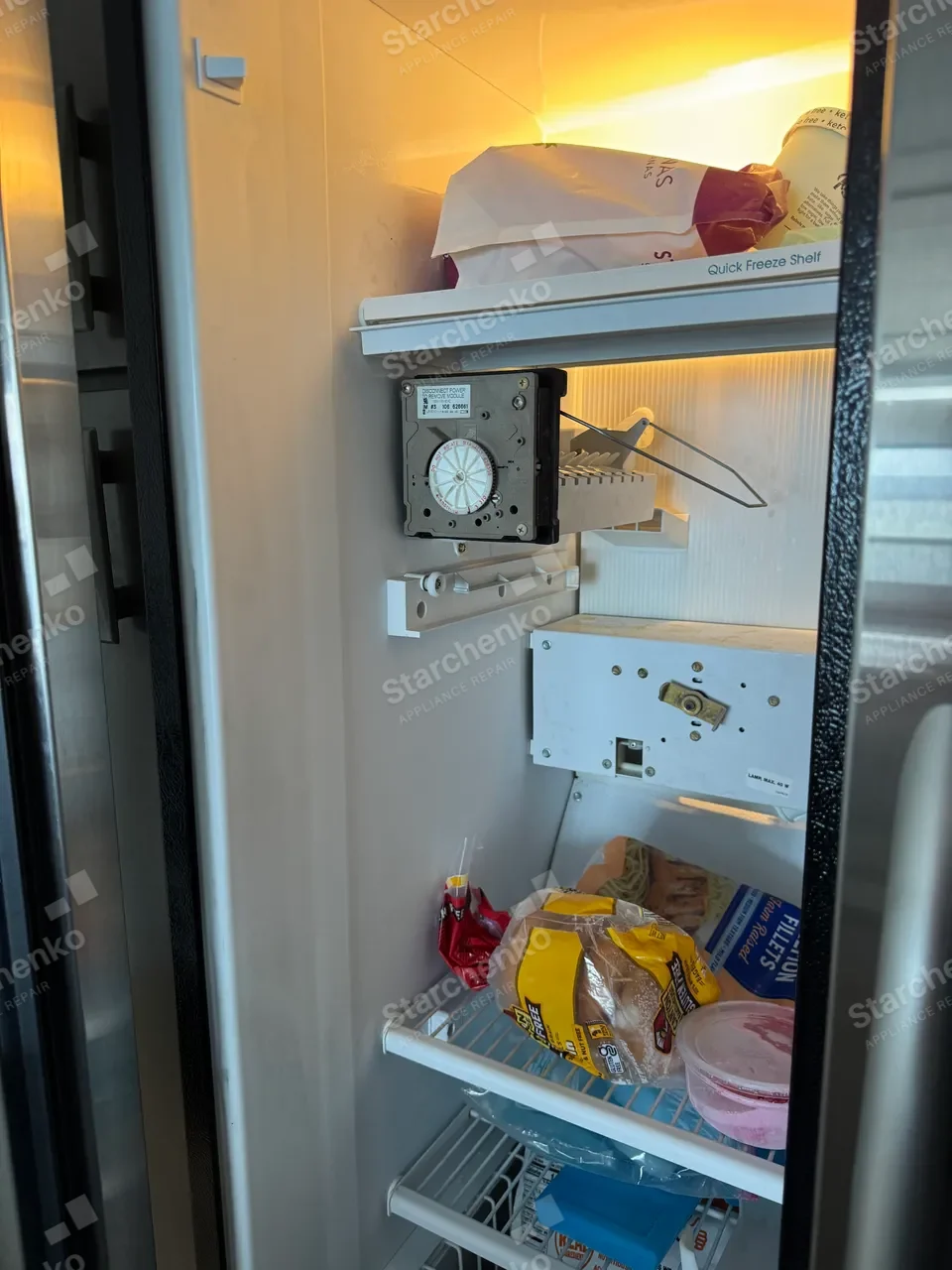KitchenAid freezer compartment of a side-by-side refrigerator with the ice maker module unbolted and resting on the shelf