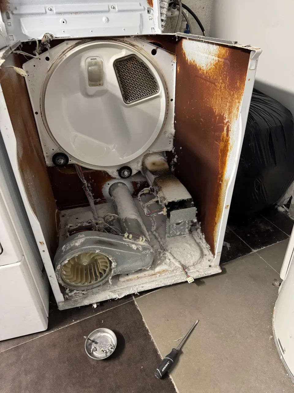 Dryer opened from the back with the drum, blower housing and heating element exposed, lint covering the cabinet
