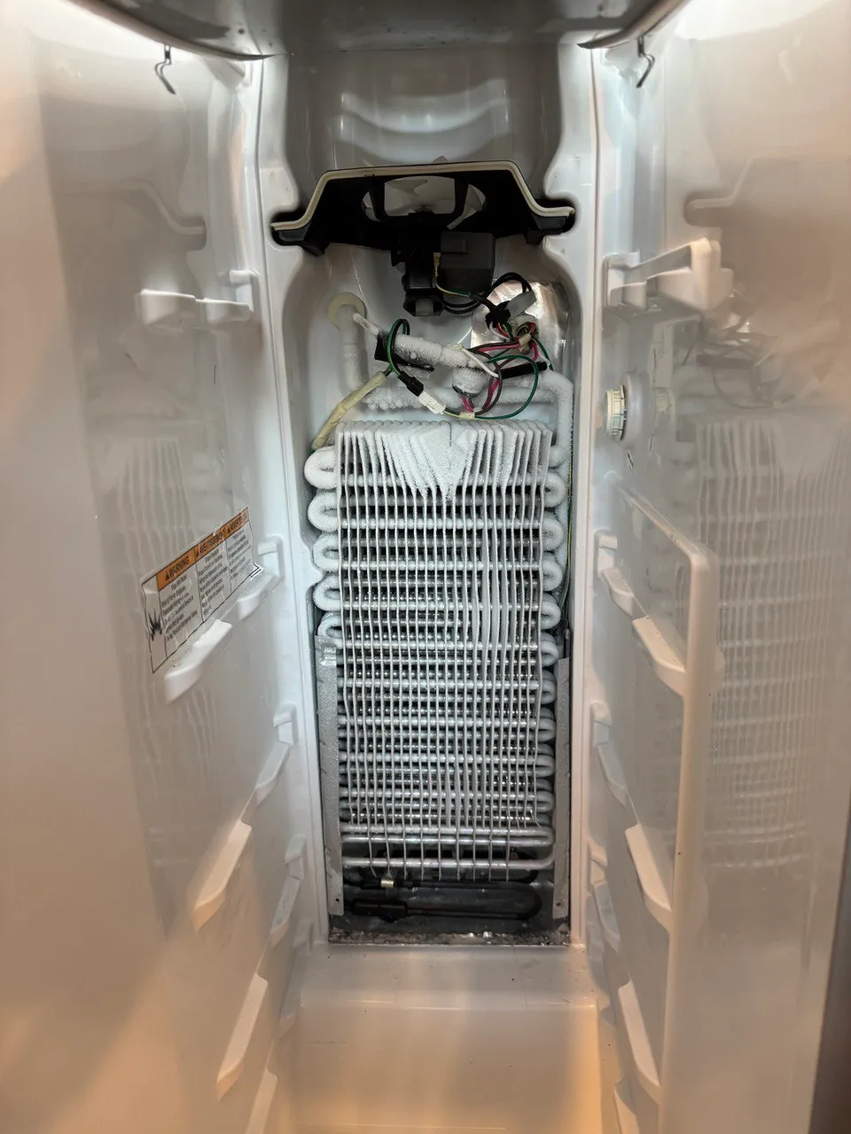Frosted Frigidaire refrigerator evaporator coil and fan housing inside an empty freezer