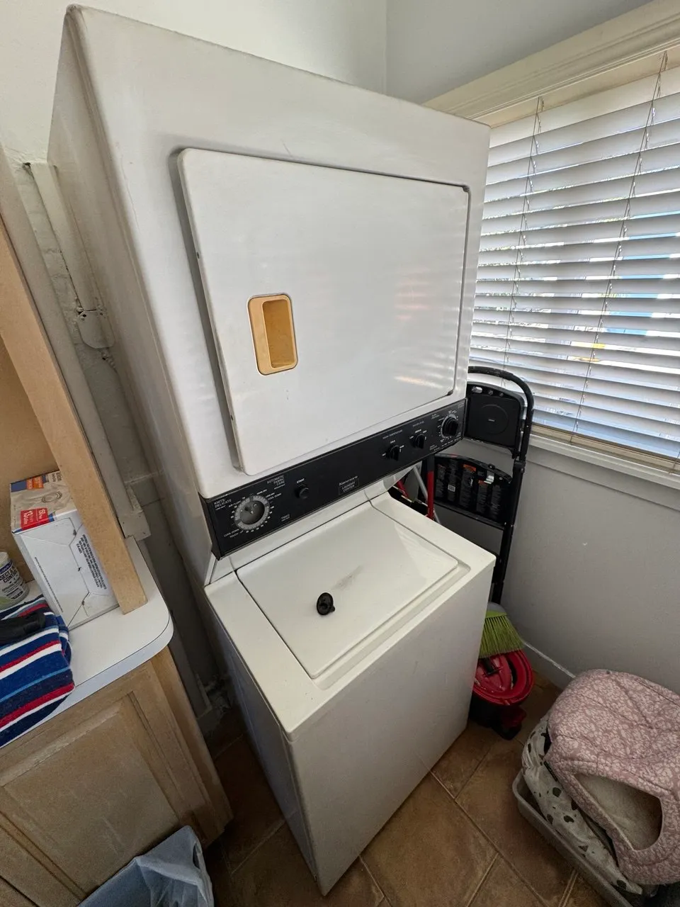 White Maytag stacked laundry center beside a window and laundry basket
