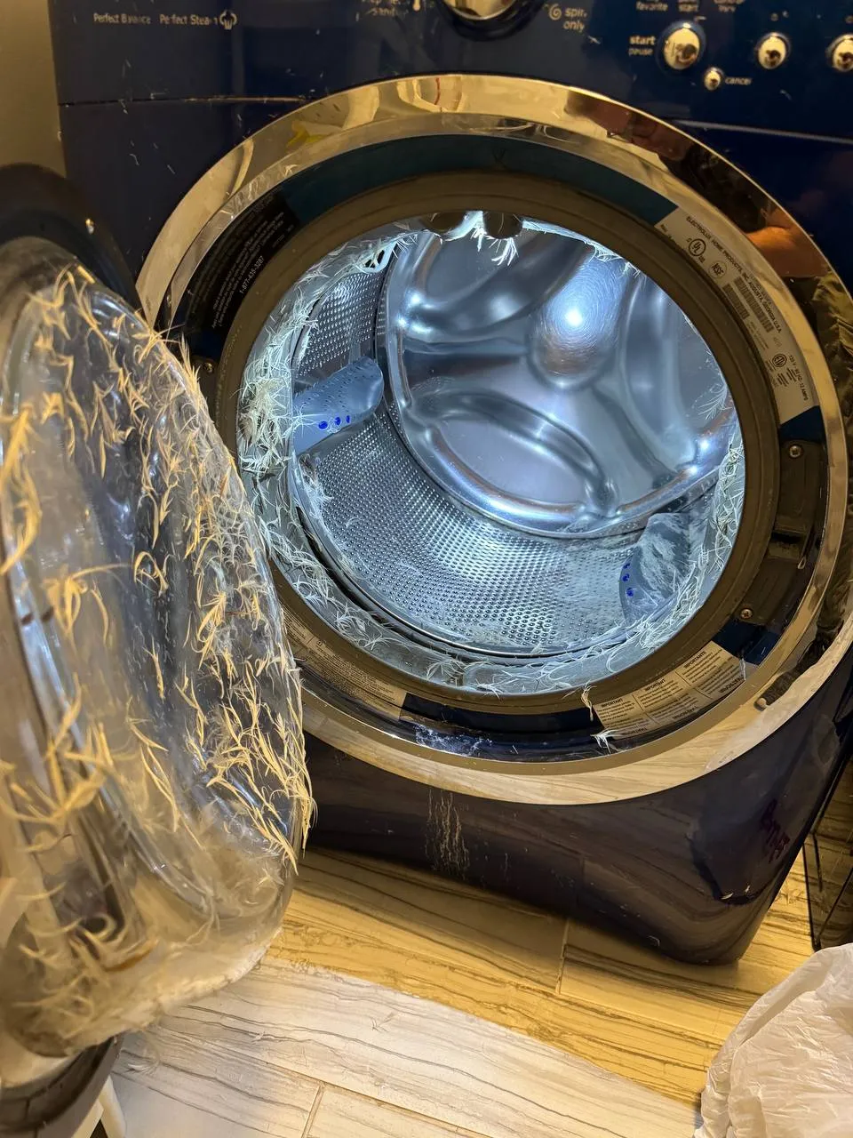 Electrolux front-load washer with the door open and burst pillow filling caught around the drum and door boot